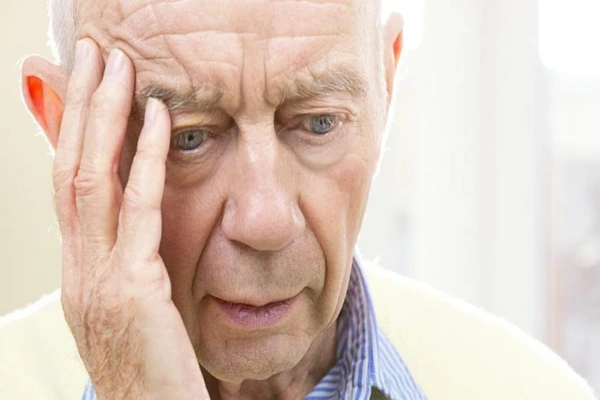 Porque Alguns Idosos Mentem: Idoso com camisola amarela clara e camisa às riscas sentado junto a uma janela, simbolizando reflexão e comportamento emocional na terceira idade.